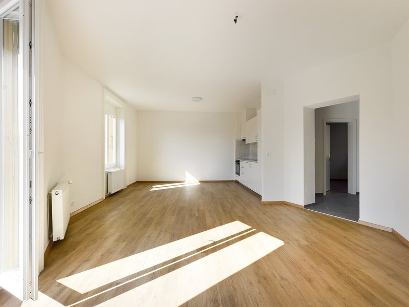 / an empty room with white walls and wooden floors and a large window letting light into the house